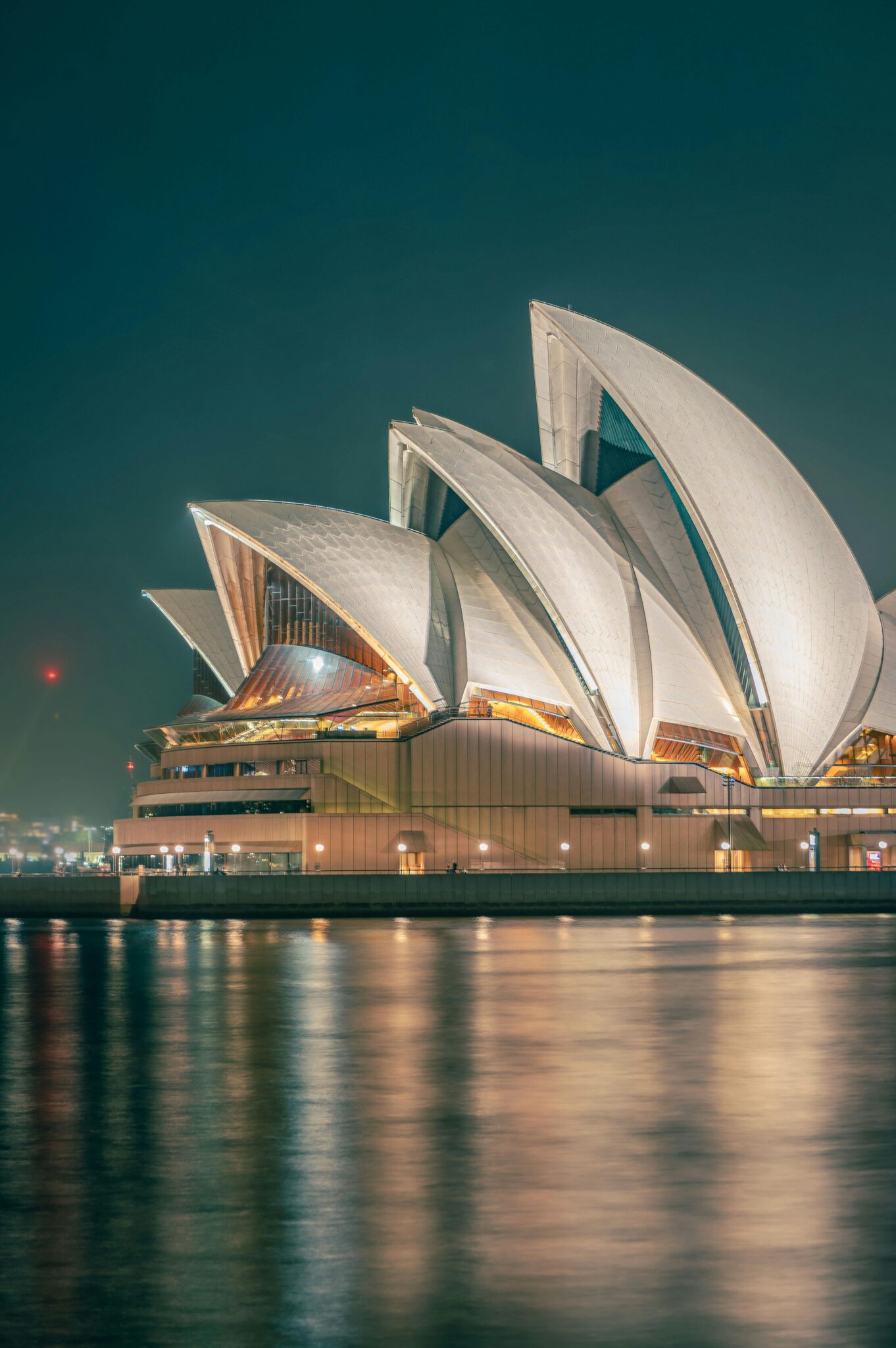 The iconic Sydney Opera House beautifully illuminated at night, reflecting on the tranquil water.